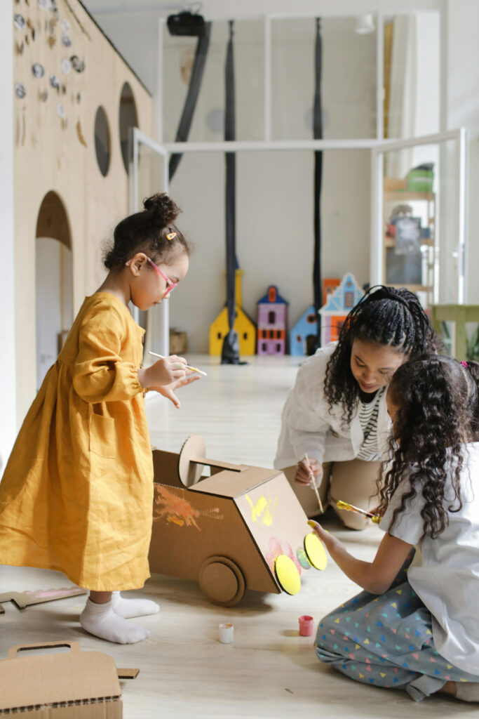 Three children painting a cardboard car