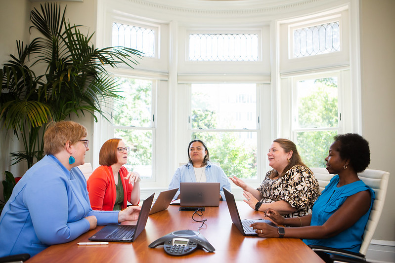 Five women sitting around a table with laptops in front of each of them